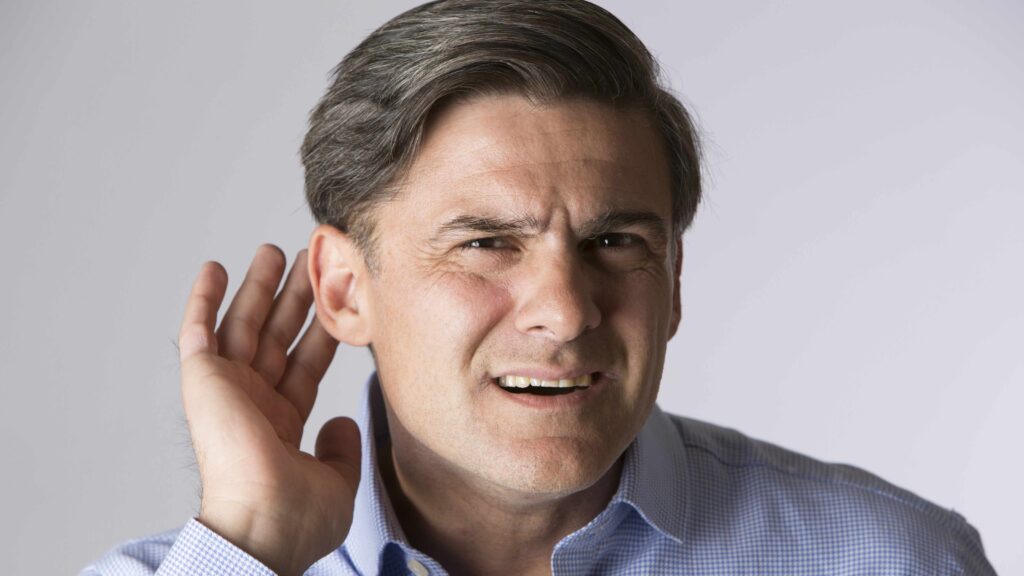 Middle-aged man struggling to hear, showing early warning signs of hearing loss.