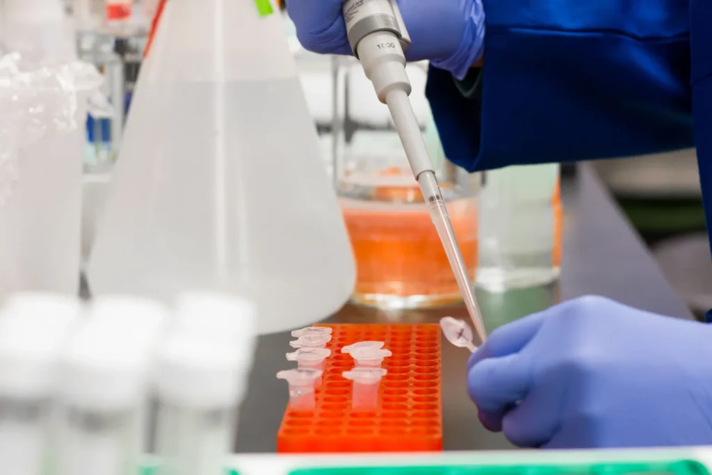 A researcher wearing gloves uses a pipette to place samples into laboratory tubes during gene therapy research
